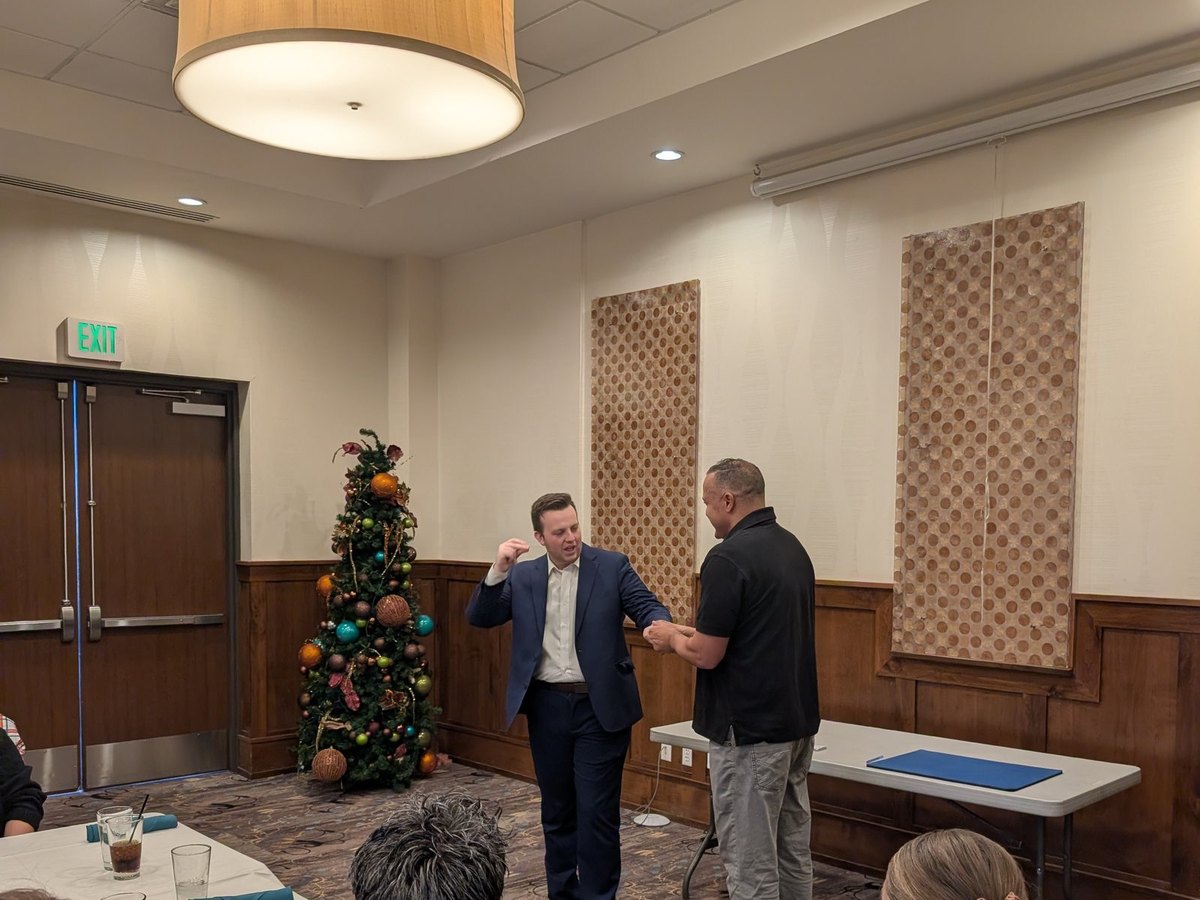 Tyler August performing beside a decorated Christmas tree at a company party