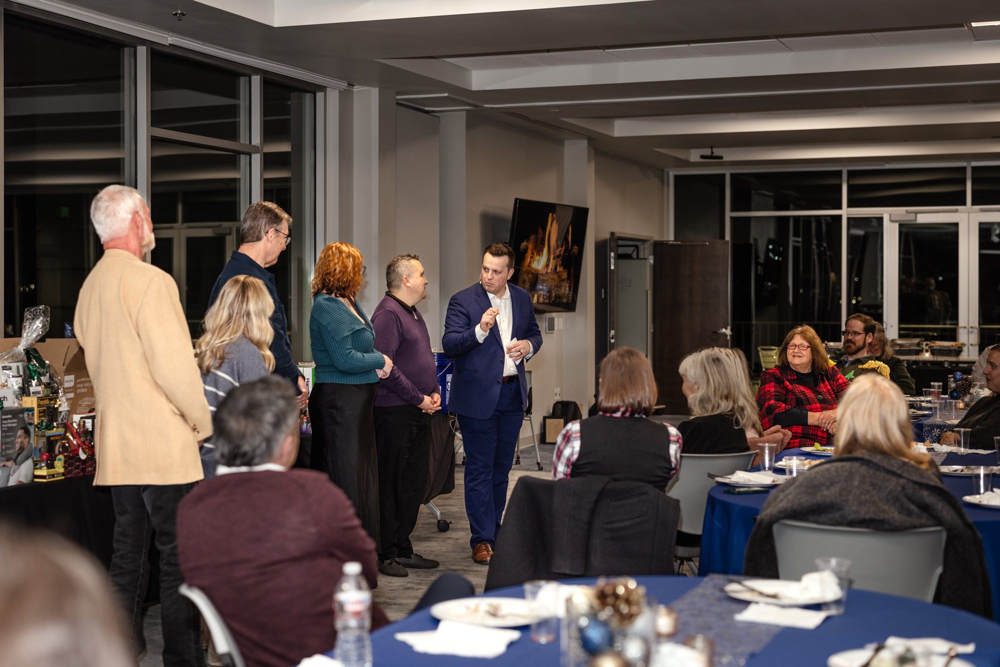 Tyler August performing for a full company holiday party, guests standing and seated around him