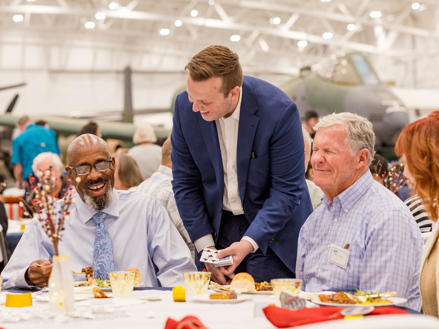 Tyler August showing a card trick to two guests laughing at their table during a USO dinner