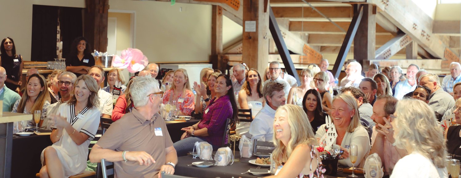 A full room of guests laughing together during Tyler August's show at the PC Tots fundraiser