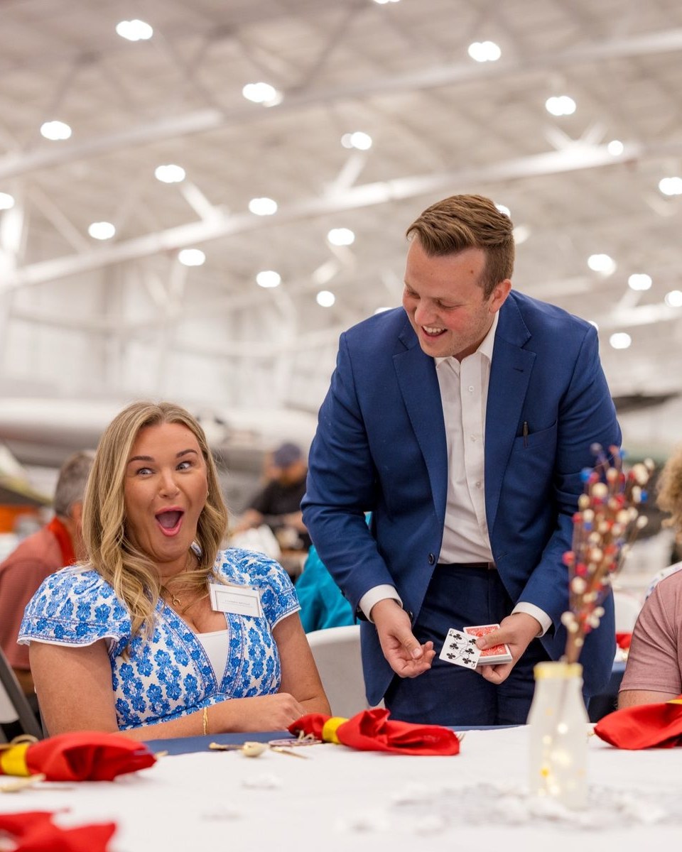 A guest reacting in shock as Tyler August performs close-up card magic at her table during a USO dinner